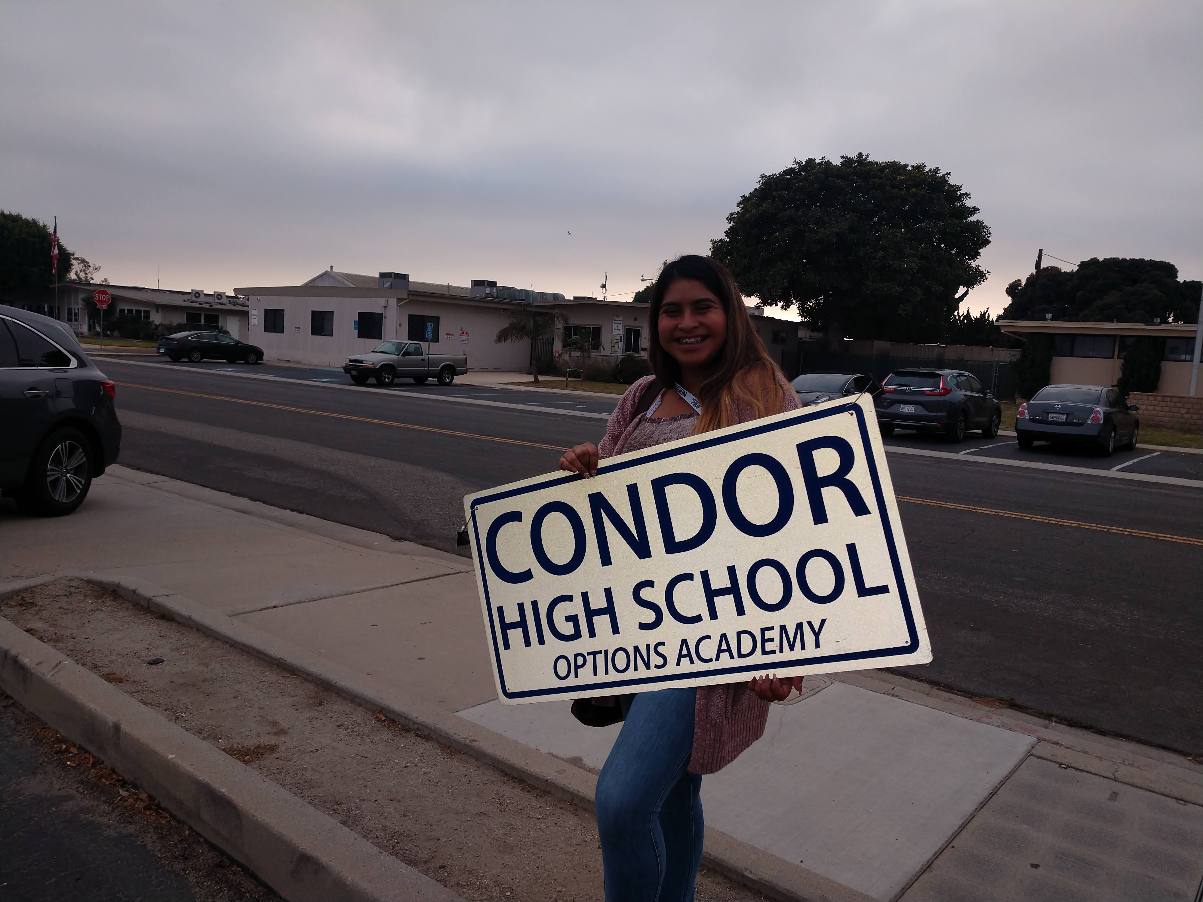 The girl is standing by the road with signboard of Condor High School